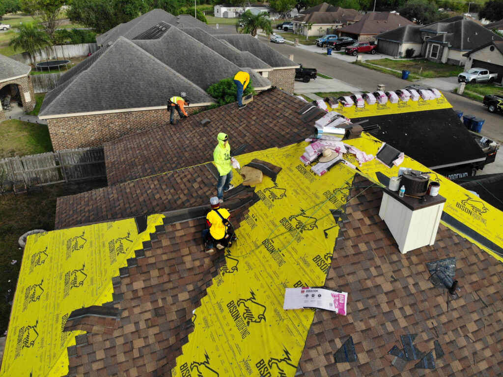 An aerial view of a professional roofing crew installing new asphalt shingles on a home in a San Antonio neighborhood, showing the yellow underlayment and architectural shingles.